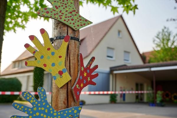 buntbemalte Hände aus Holz und im Hintergrund der Kindergarten Bergstraße